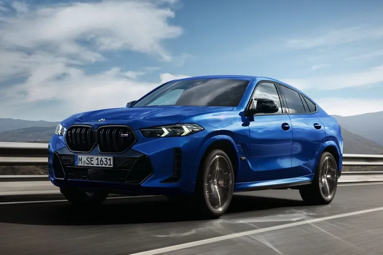 A BMW X6 SUV is driving down a motorway in front of a mountain vista