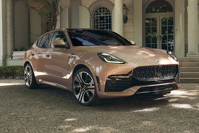 A metallic rose gold Maserati Grecale SUV parked on a gravel driveway in front of a building.