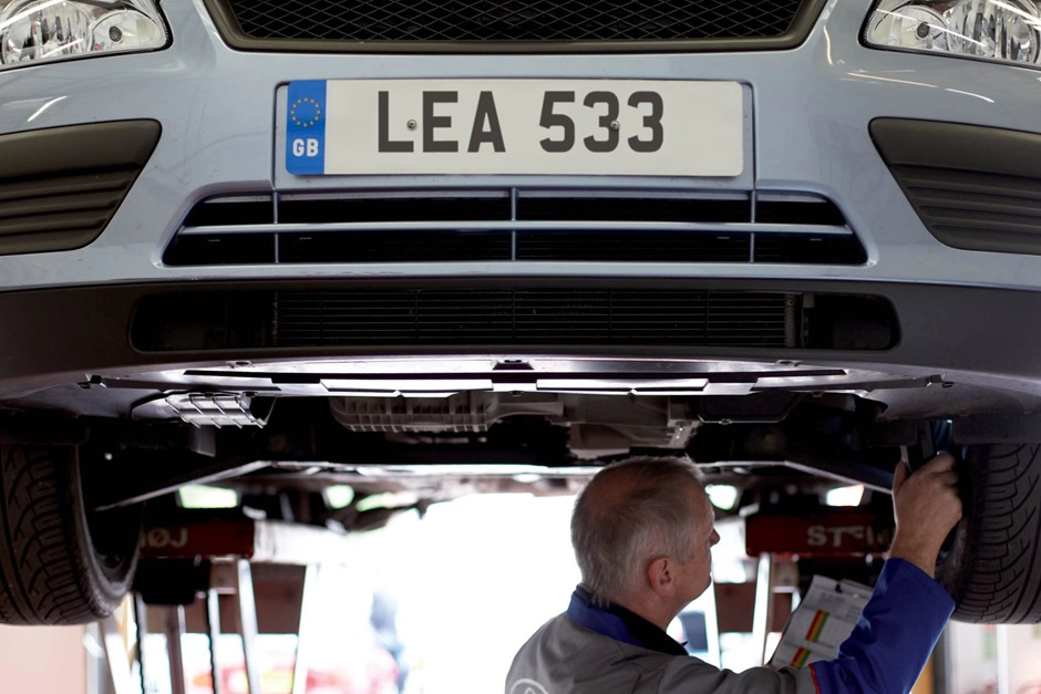 A mechanic conducts maintenance while inspecting the underside of a car.
