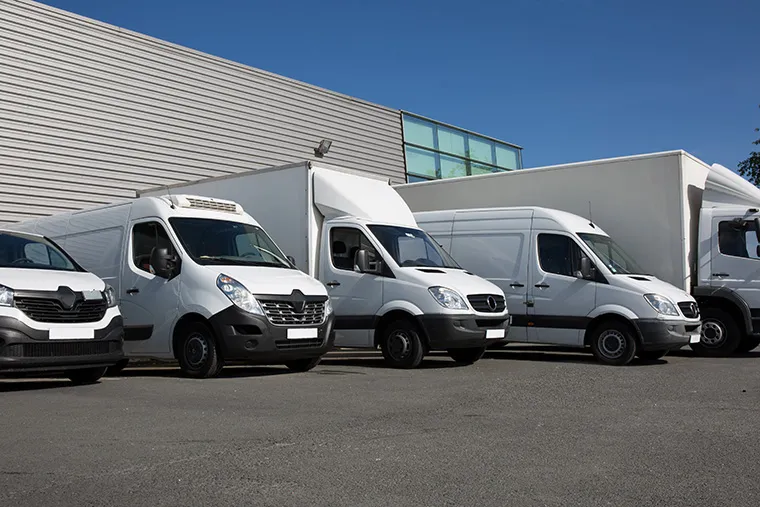 A line-up of white commercial vans, including models from Renault, Mercedes, and other popular brands, parked outside a building. This image highlights a variety of options for businesses seeking reliable van leasing solutions.