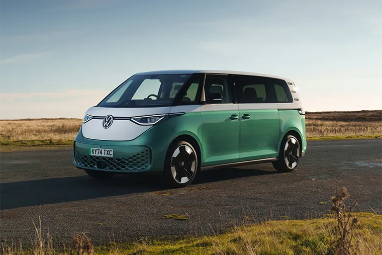 A side view of a green and white Volkswagen ID. Buzz electric van parked on an open road with a scenic backdrop. The vehicle showcases its modern design, perfect for businesses looking for eco-friendly and stylish van leasing options.