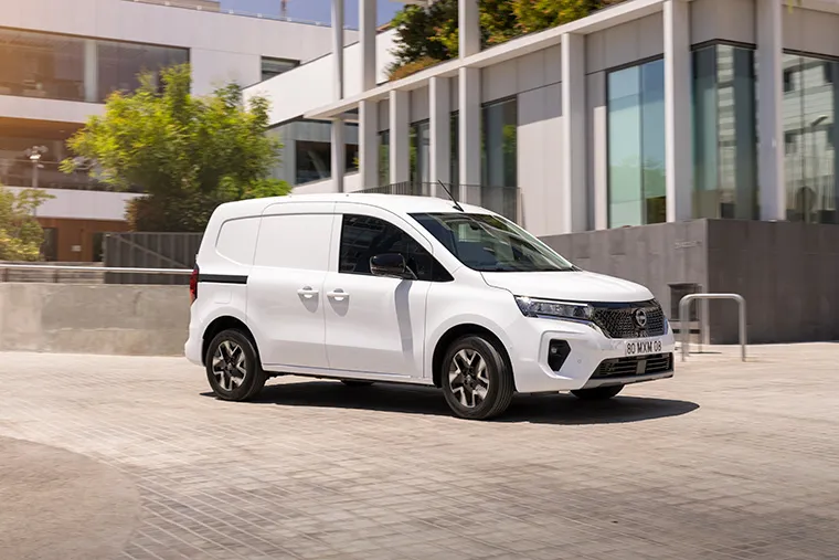 A white Nissan Townstar van parked in front of a modern building.
