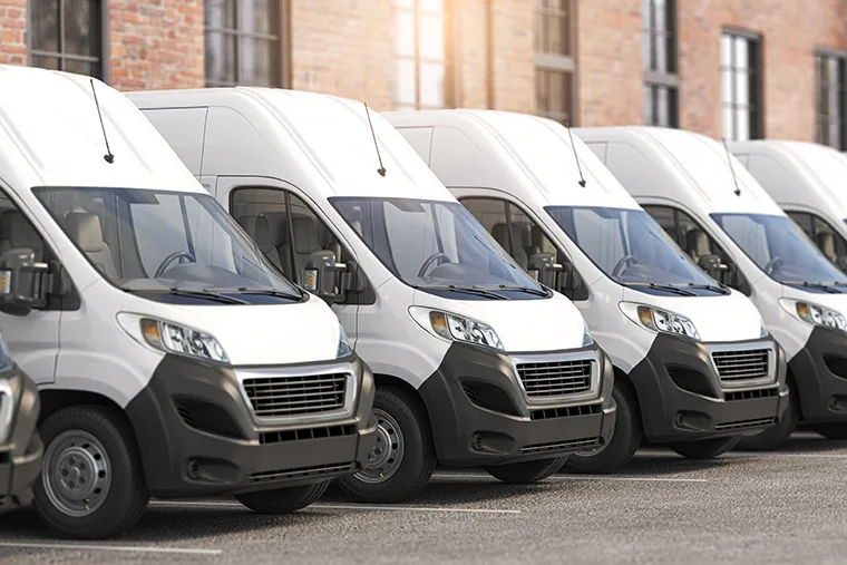Row of white commercial vans lined up in a parking lot, showcasing their sturdy design and suitability for business needs.