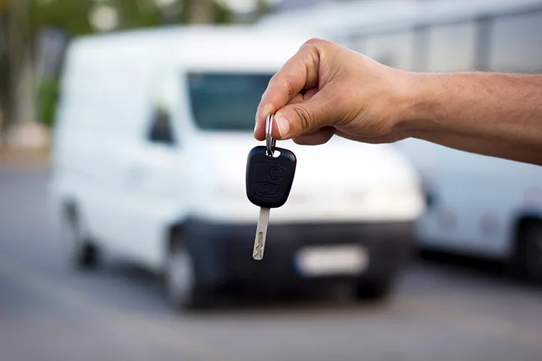 A hand holding a set of keys in front of a white commercial van