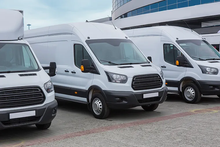 A row of white commercial vans, featuring different models parked outside a building.