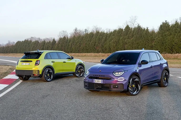 Two Abarth 600e electric SUVs—one in vibrant green and the other in deep purple parked.