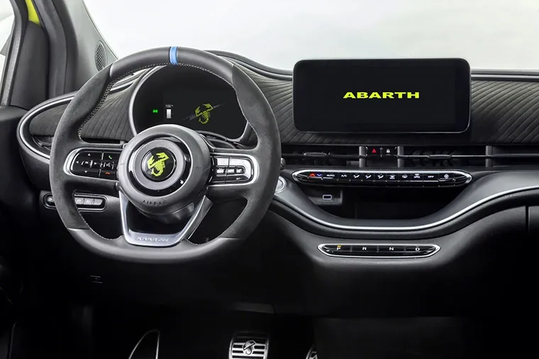 Interior view of an Abarth electric car showing the digital cockpit with Abarth scorpion logo on the steering wheel and dashboard screen, highlighting sporty design details.