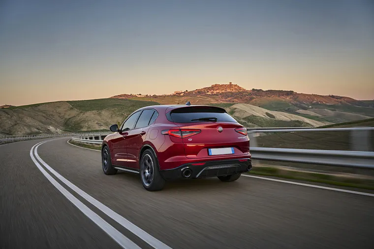 Red Alfa Romeo Stelvio driving on mountain road rear view