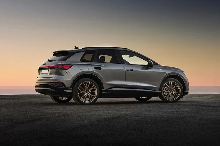 Audi Q6 e-tron SUV in blue driving through scenic mountain road.