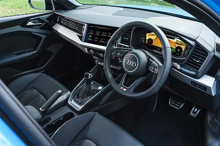 Blue Audi A1 Sportback driving on country road, showcasing Audi's compact premium hatchback with sporty styling.