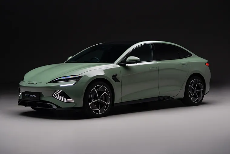 Side view of a BYD Seal electric saloon car in a studio setting, showcasing its sleek, aerodynamic shape, futuristic alloy wheels, and illuminated front LED lights.