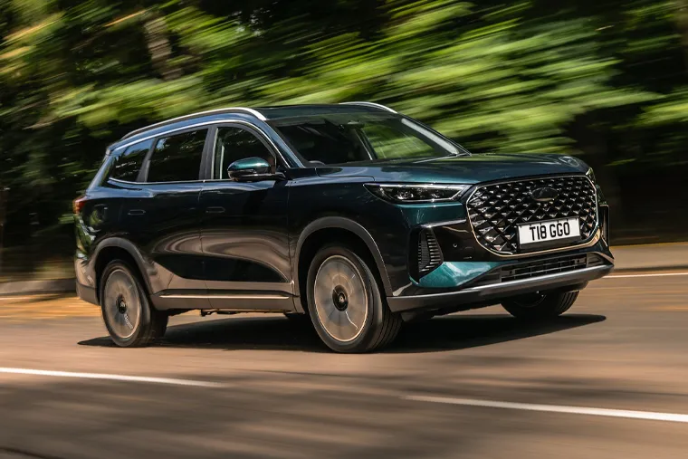 Dark green Chery SUV in motion on a woodland road, emphasising its sculpted exterior, large alloy wheels and contemporary SUV design.