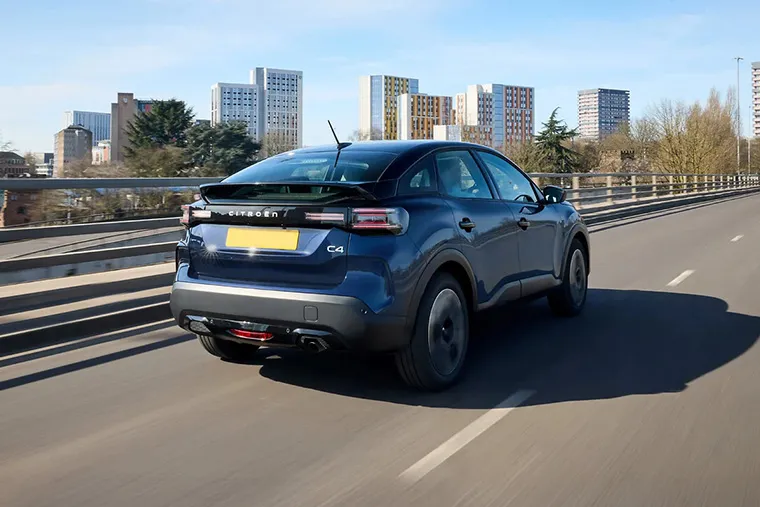 Citroen C4 crossover SUV driving on urban highway with city skyline in the background.