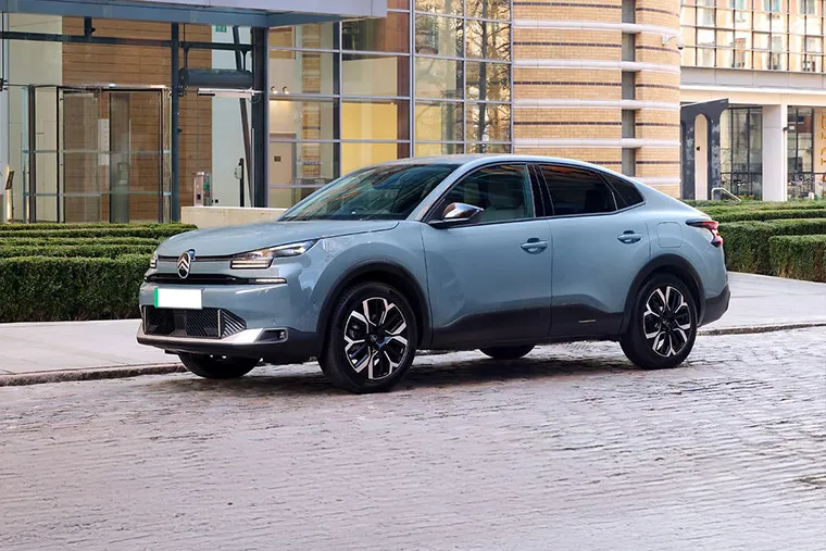 Citroen e-C4 X parked outside a modern glass office building, showcasing sleek coupe SUV styling.