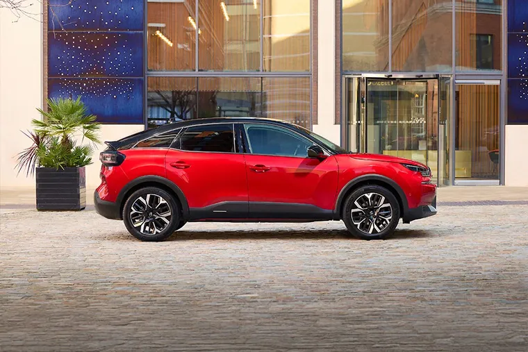 Citroen e-C4 X electric SUV in red parked in front of a modern glass building in an urban setting.