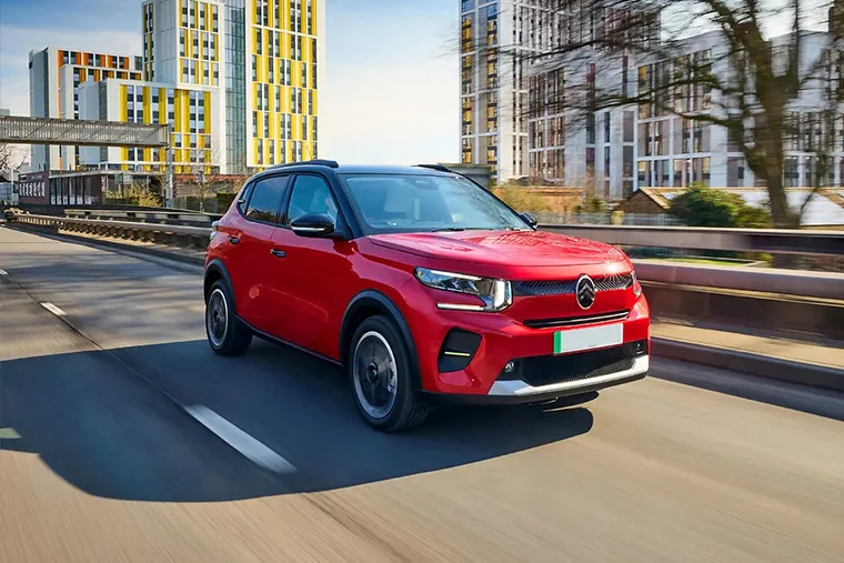 Red Citroen C3 Aircross SUV driving through modern cityscape with urban high-rises in the background.