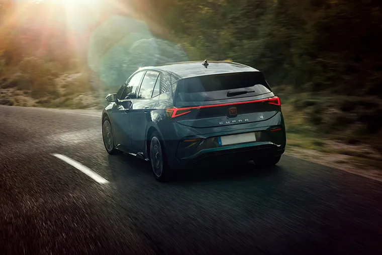 Rear view of the Cupra Born electric hatchback driving through forest roads at sunrise, highlighting its LED tail lights and aerodynamic design.