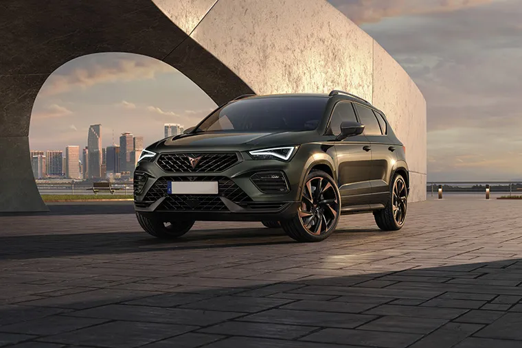 Cupra Ateca SUV parked beneath an architectural archway at dusk, set against a modern urban skyline.