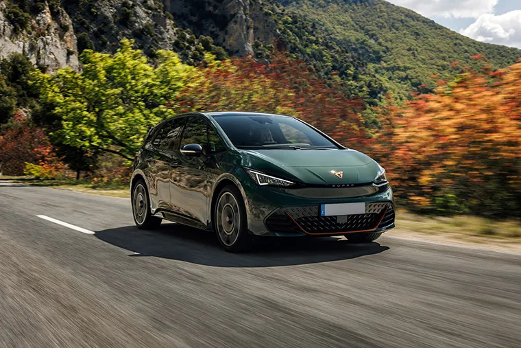 Cupra Born electric hatchback in racing green driving through a forest road in autumn.