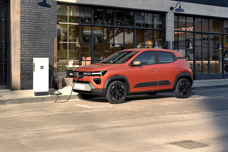 Electric Dacia parked and charging near a café on an urban street
