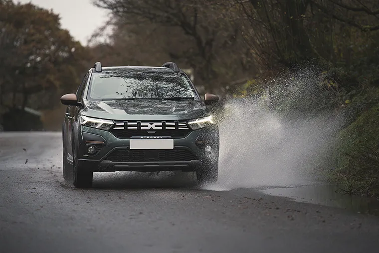 Dacia Stepway driving through a puddle on a wet country road
