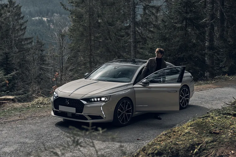 DS 9 luxury saloon parked in forest with driver standing beside car