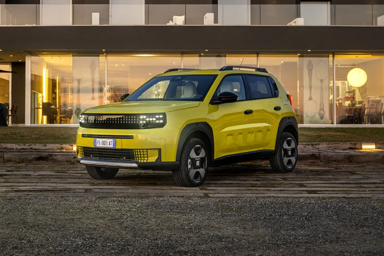 Fiat Panda electric SUV in yellow parked in front of modern luxury house at sunset.