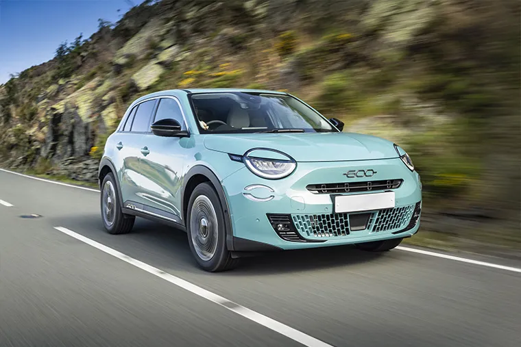 Fiat 600e electric SUV in mint green driving on a scenic mountain road.
