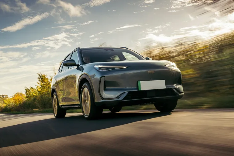 Geely electric SUV in dark grey driving dynamically on a rural road with motion-blurred background trees and dramatic sky