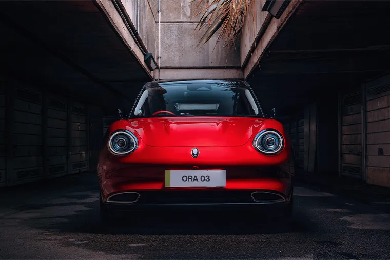 Red ORA 03 electric hatchback front view parked in a dimly lit urban setting