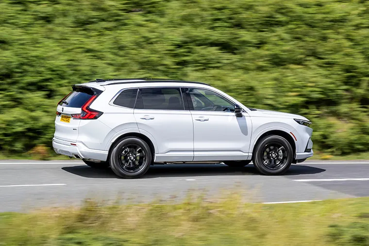 White Honda SUV driving on a countryside road with green foliage in the background