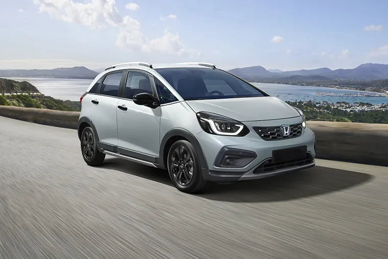 White Honda Jazz Crosstar driving along a scenic coastal mountain road under a bright blue sky