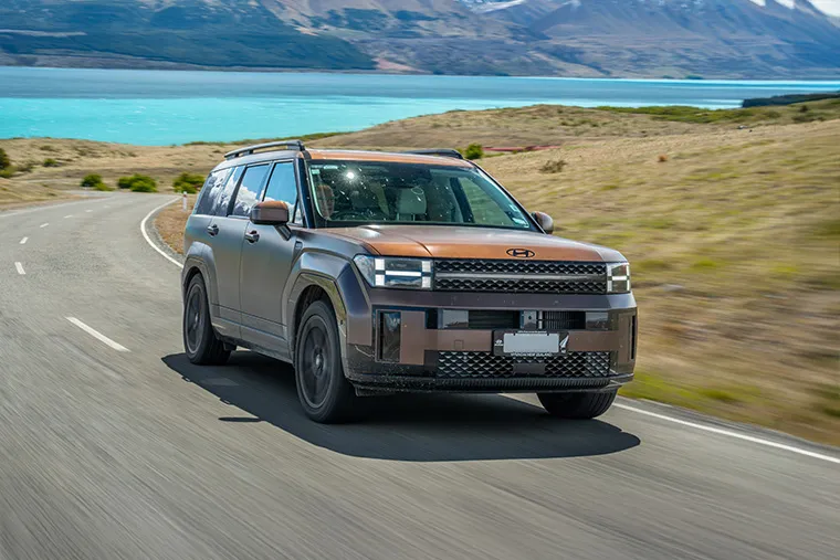 Hyundai SUV driving on a scenic coastal road with mountains and lake in the background.