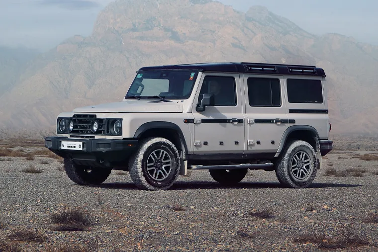 INEOS Grenadier off‑road SUV parked on rocky desert terrain with mountains behind, emphasising durability, adventure performance and rugged build.