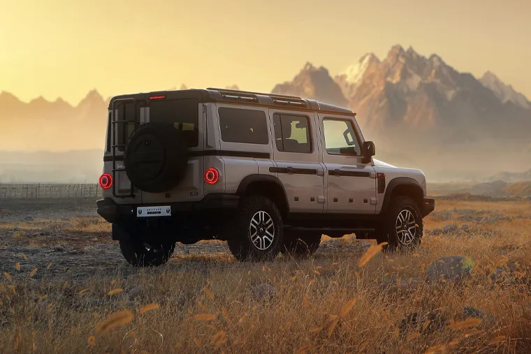 Rear view of INEOS Grenadier SUV at sunset in mountainous landscape, highlighting tough exterior styling, spare wheel mount and off‑road capability.