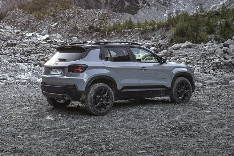 Jeep Avenger SUV parked on rocky terrain with towering mountains and sunset in the background.