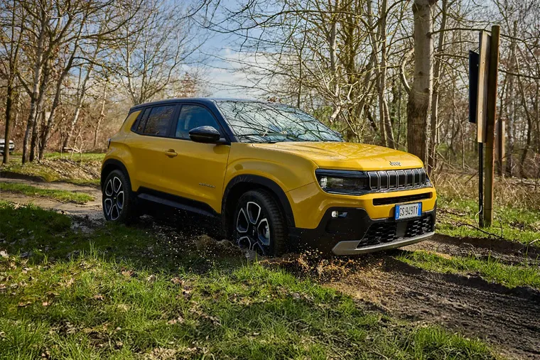 Yellow Jeep Avenger electric SUV driving through countryside with vineyards in the background.