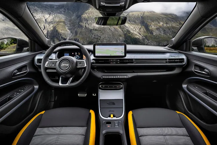 Modern Jeep interior cabin view with digital dashboard, touchscreen navigation, and yellow-accented seats against a mountain backdrop.