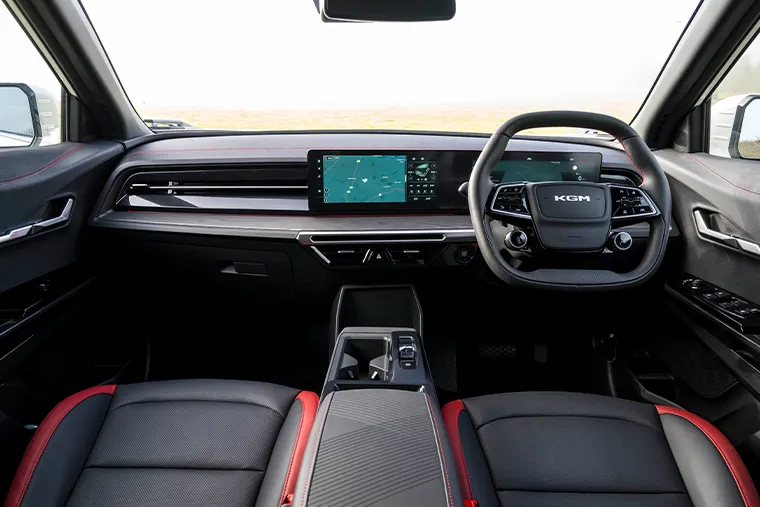 Interior of a KGM SUV featuring a widescreen infotainment display, modern steering wheel with KGM logo, and black leather seats with red stitching