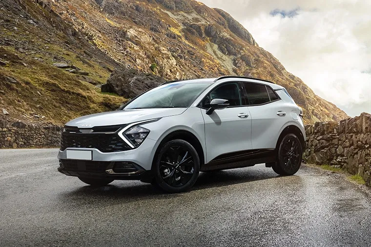 White Kia Sportage SUV parked on a scenic mountain road, showcasing its rugged styling and practicality for drivers.