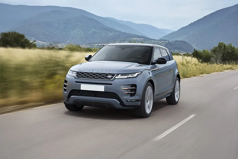 Grey Range Rover Evoque driving on open country road with mountain backdrop.