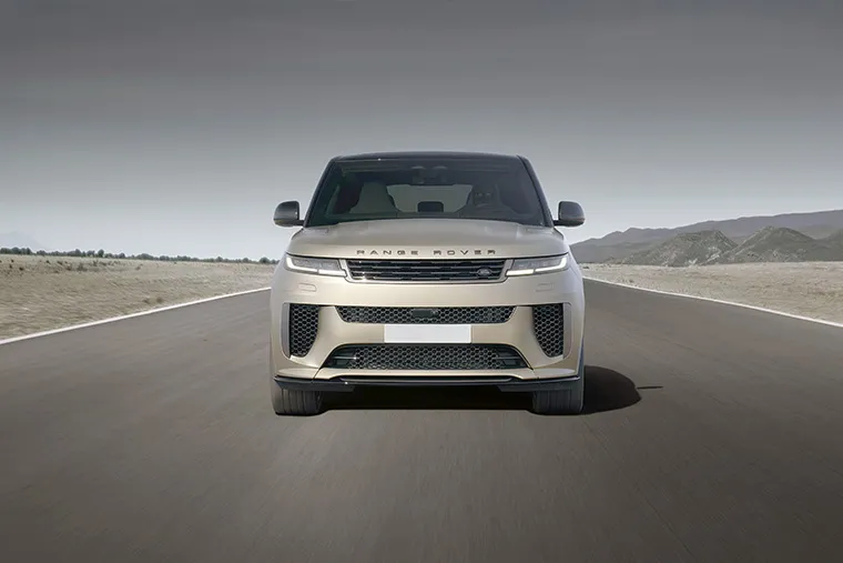 Front view of a gold Range Rover driving on open road at dusk, with mountains in the background.