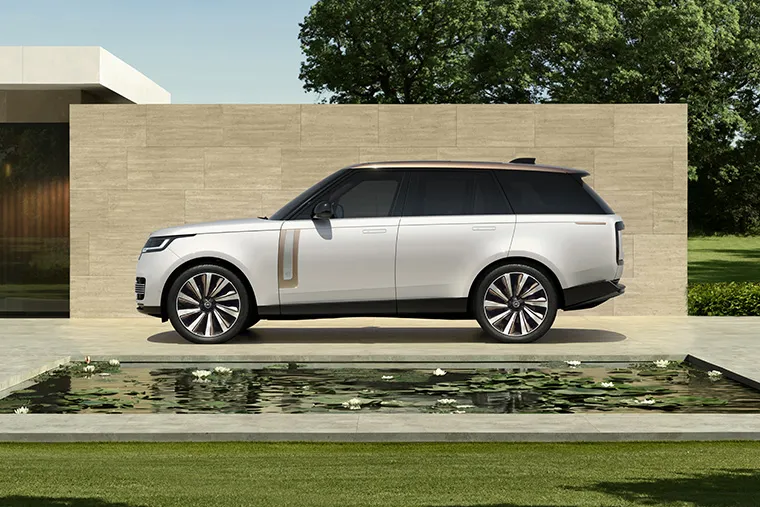 Side view of a white Range Rover parked beside a modern house with reflecting pond.