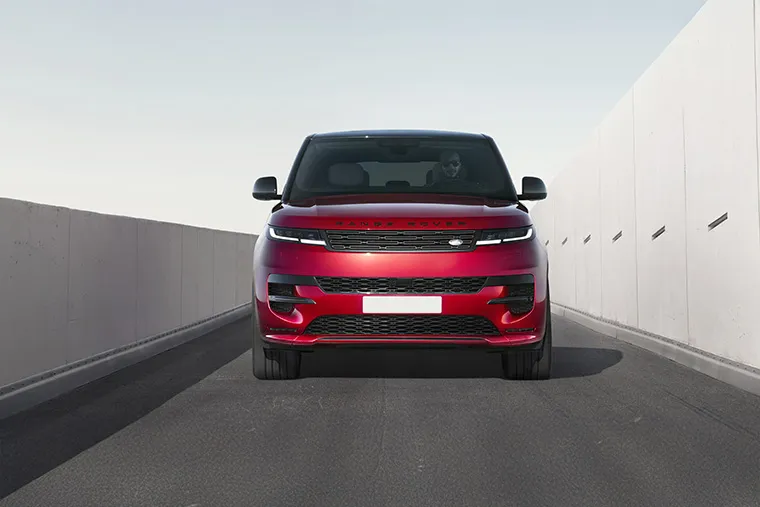 Front view of a red Range Rover SUV on a clean urban road with minimalist concrete walls.