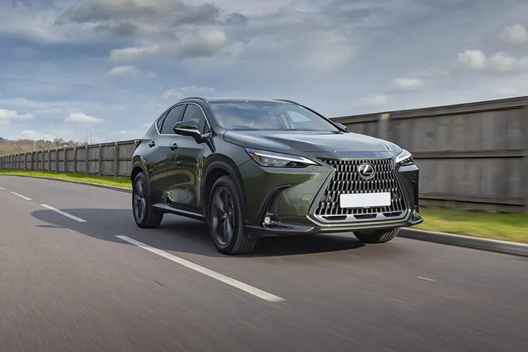 A green Lexus NX driving on a suburban road, highlighting its bold front grille and dynamic SUV profile under a cloudy sky.
