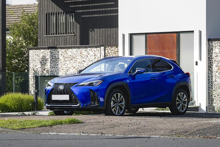 A blue Lexus UX 300e parked in front of a modern house, showcasing its sleek design and electric badge in a residential setting.
