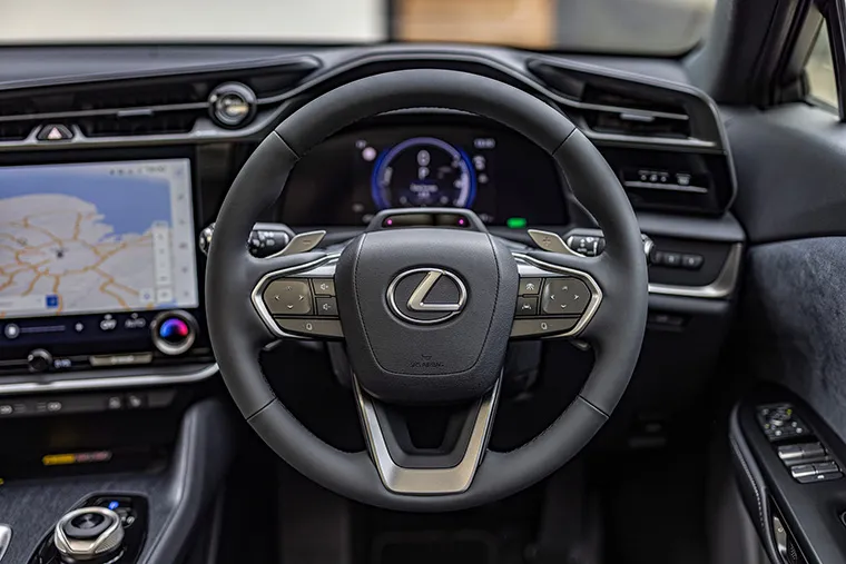 Interior close-up of a modern Lexus showing the steering wheel with Lexus logo, a digital driver display, and a wide infotainment touchscreen with built-in navigation.