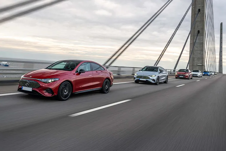 Line of Mercedes-Benz EQE and C-Class models driving across a suspension bridge on a cloudy day