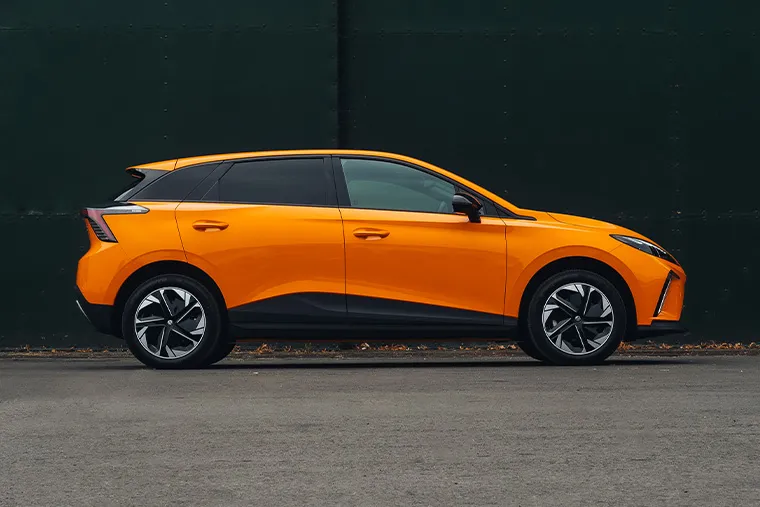 Side profile of 2025 MG4 EV hatchback in bright orange parked outdoors