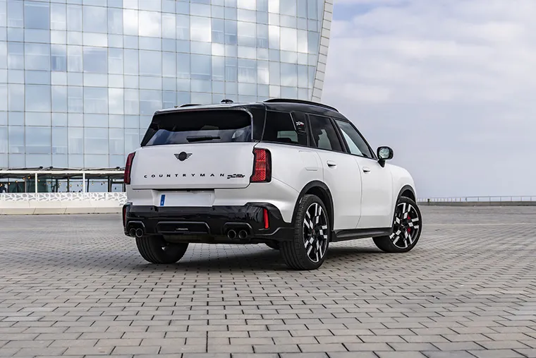 White MINI Countryman SE parked on a modern paved plaza with a glass-fronted skyscraper in the background.